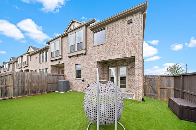 rear view of property with a residential view, central AC, brick siding, a fenced backyard, and a yard