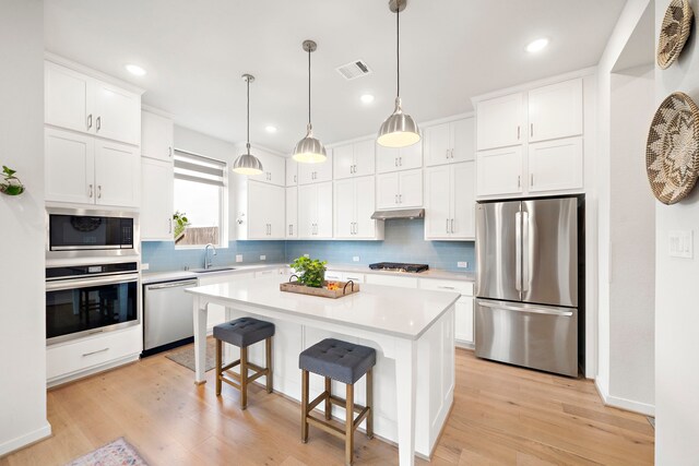 kitchen featuring under cabinet range hood, appliances with stainless steel finishes, decorative backsplash, and visible vents