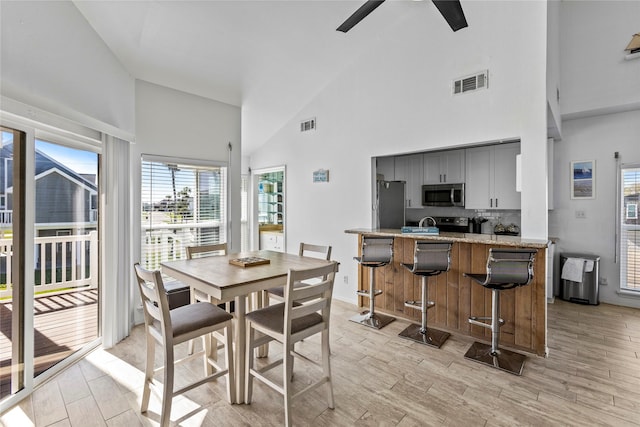 dining room with visible vents, a healthy amount of sunlight, ceiling fan, and high vaulted ceiling
