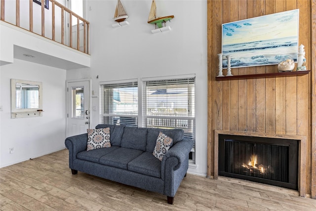 living room featuring visible vents, wood finished floors, a warm lit fireplace, and a towering ceiling