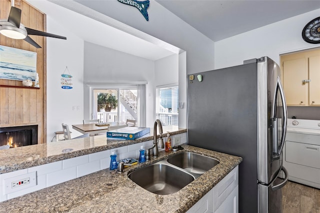 kitchen featuring dark stone counters, a sink, washer / dryer, a lit fireplace, and wood finished floors