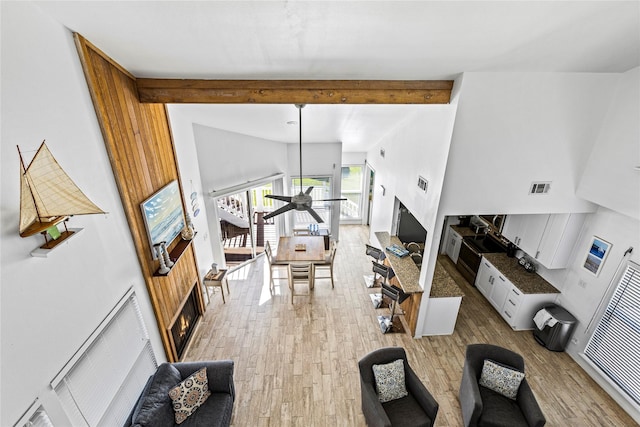 living room with light wood finished floors, a high ceiling, beam ceiling, ceiling fan, and visible vents