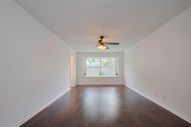 empty room featuring dark wood-style flooring, a ceiling fan, and baseboards