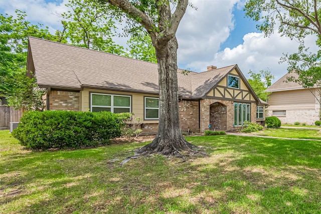english style home with a front lawn, fence, a shingled roof, and brick siding