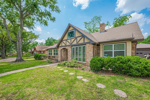 tudor-style house with a chimney, brick siding, a shingled roof, and a front yard