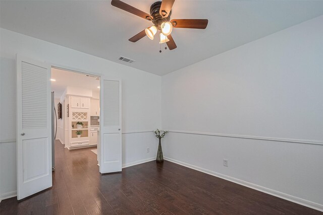unfurnished room with dark wood-style floors, visible vents, a ceiling fan, and baseboards