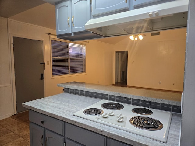 kitchen with white electric cooktop, dark tile patterned flooring, under cabinet range hood, and light countertops