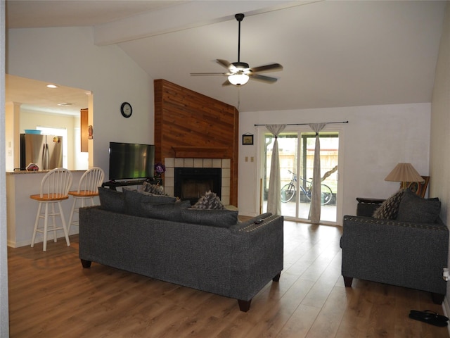 living area with a tiled fireplace, lofted ceiling with beams, a ceiling fan, and wood finished floors
