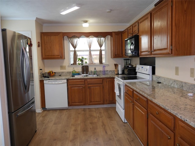 kitchen with brown cabinetry, white appliances, light wood-type flooring, light stone counters, and a sink