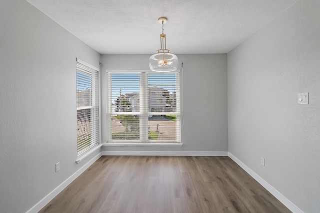 unfurnished dining area featuring a textured ceiling, wood finished floors, and baseboards