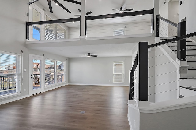 unfurnished living room featuring wood finished floors, baseboards, stairway, a ceiling fan, and a towering ceiling