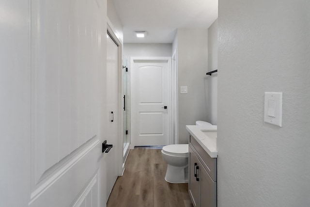 bathroom with a textured wall, a stall shower, toilet, wood finished floors, and vanity