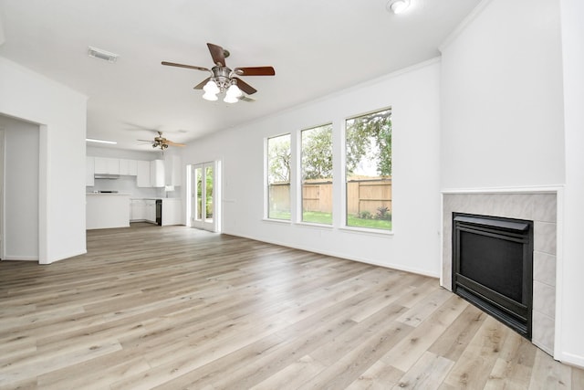 unfurnished living room featuring light wood-style flooring, ceiling fan, a fireplace, visible vents, and crown molding