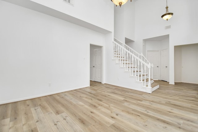 unfurnished living room featuring wood finished floors, stairs, baseboards, visible vents, and a towering ceiling