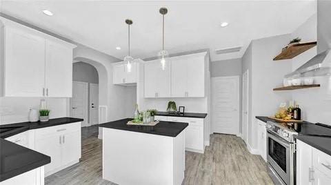 kitchen with stainless steel electric range oven, open shelves, dark countertops, arched walkways, and a center island