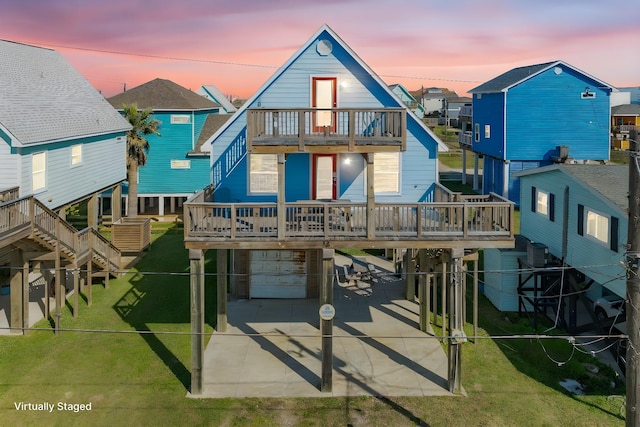 back of house at dusk with driveway, a carport, a balcony, an attached garage, and a yard