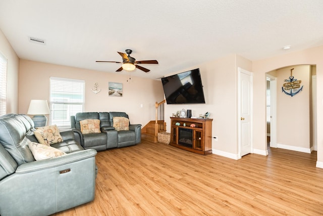living area featuring light wood-style flooring, visible vents, arched walkways, baseboards, and a ceiling fan