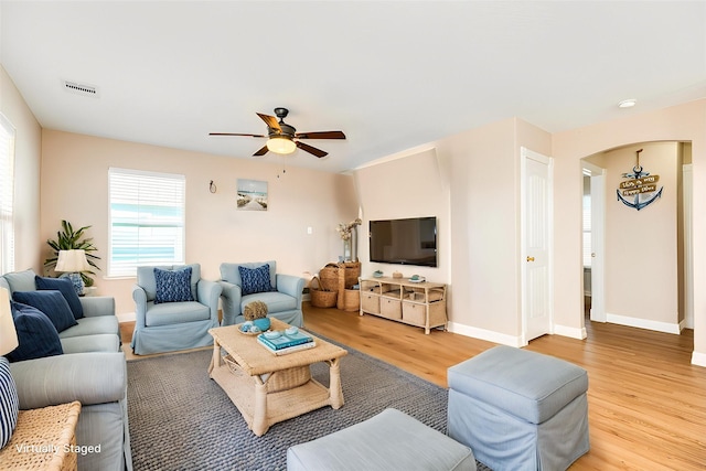 living area with arched walkways, light wood finished floors, baseboards, visible vents, and a ceiling fan