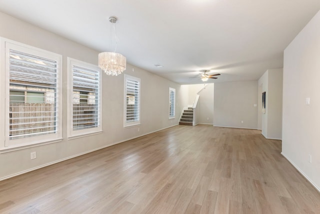 549 Timber Voyage Ct, Conroe, TX 77304 - unfurnished living room featuring baseboards, light wood-style flooring, ceiling fan with notable chandelier, and stairway
