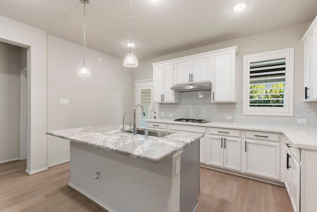549 Timber Voyage Ct, Conroe, TX 77304 - kitchen featuring tasteful backsplash, light wood-type flooring, gas stovetop, a sink, and under cabinet range hood