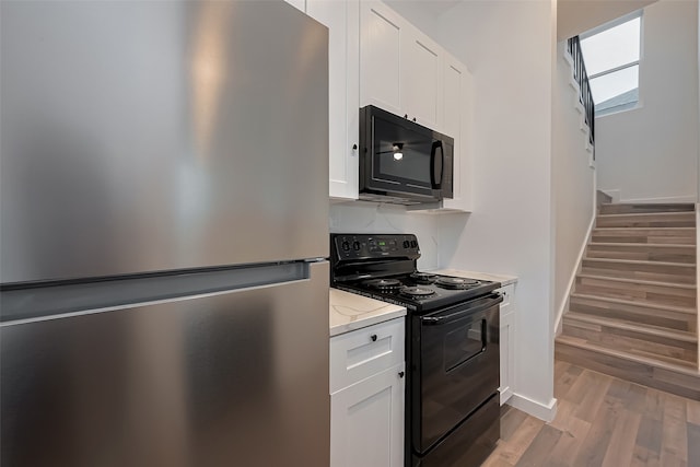9003 Hilda St, Houston, TX 77033 - kitchen with black appliances, light wood finished floors, white cabinetry, light stone countertops, and baseboards