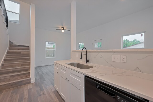 9003 Hilda St, Houston, TX 77033 - kitchen with black dishwasher, a sink, light stone counters, white cabinets, and light wood finished floors