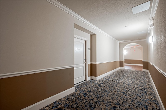 hall featuring arched walkways, ornamental molding, carpet flooring, baseboards, and a textured ceiling