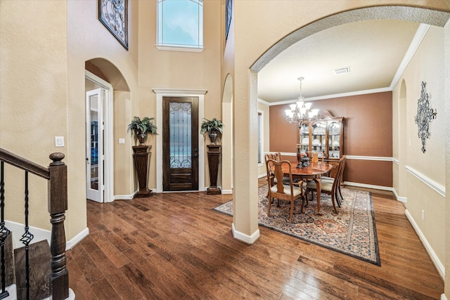 entryway with a chandelier, crown molding, wood-type flooring, and arched walkways