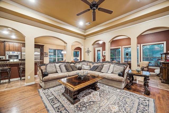living area featuring a raised ceiling, a ceiling fan, light wood-style floors, and crown molding
