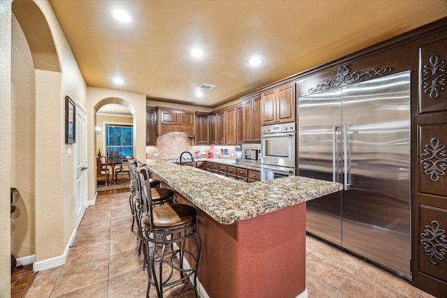 36927 Anglers Way, Pinehurst, TX 77362 - kitchen with built in appliances, arched walkways, recessed lighting, a breakfast bar area, and light tile patterned flooring