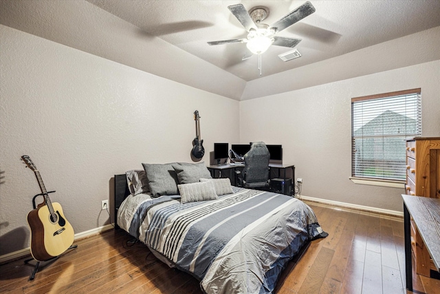bedroom featuring ceiling fan, wood-type flooring, a textured wall, baseboards, and visible vents