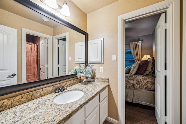ensuite bathroom featuring wood finished floors, connected bathroom, a textured wall, vanity, and baseboards