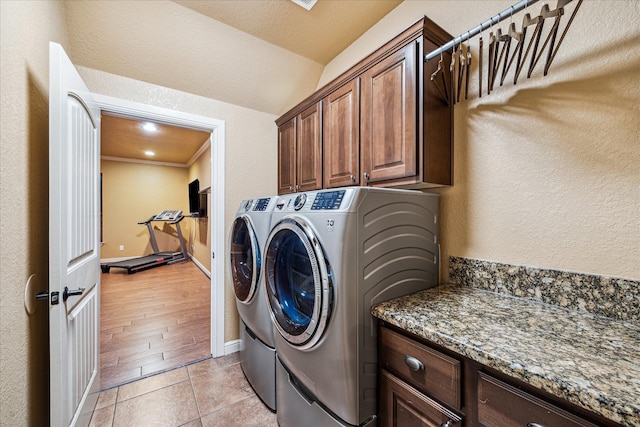 washroom featuring light tile patterned floors, separate washer and dryer, cabinet space, and a textured wall