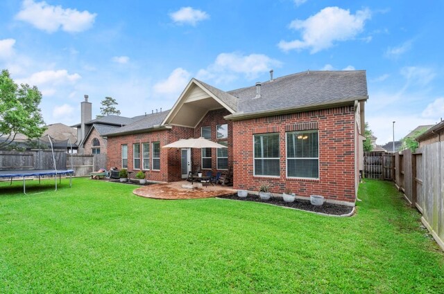 back of house with brick siding, a fenced backyard, a trampoline, and a lawn