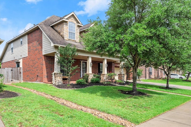 view of front facade with fence, a shingled roof, a front lawn, brick siding, and covered porch