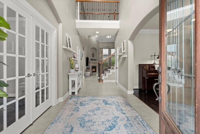 tiled foyer featuring crown molding, arched walkways, baseboards, and french doors