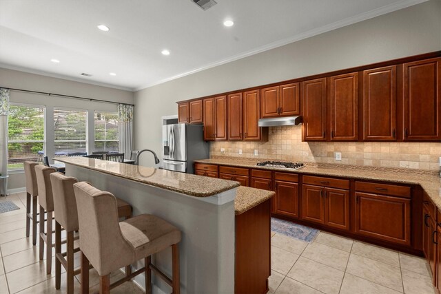 kitchen with appliances with stainless steel finishes, under cabinet range hood, a breakfast bar, and tasteful backsplash
