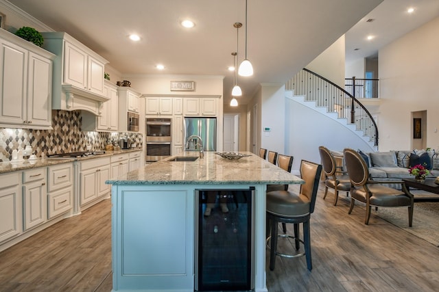 kitchen with a sink, stainless steel appliances, wine cooler, a kitchen bar, and wood finished floors