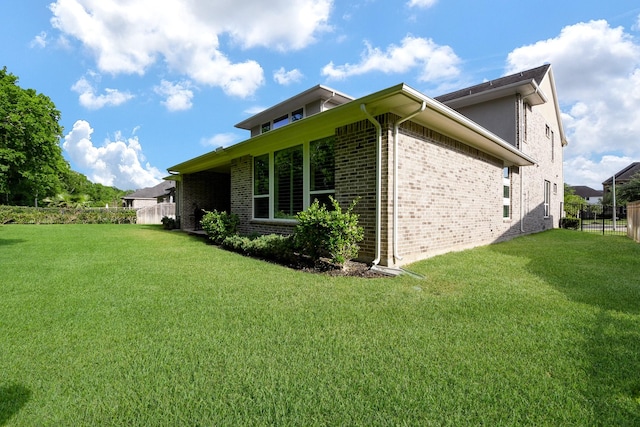 view of side of home with fence, a lawn, and brick siding