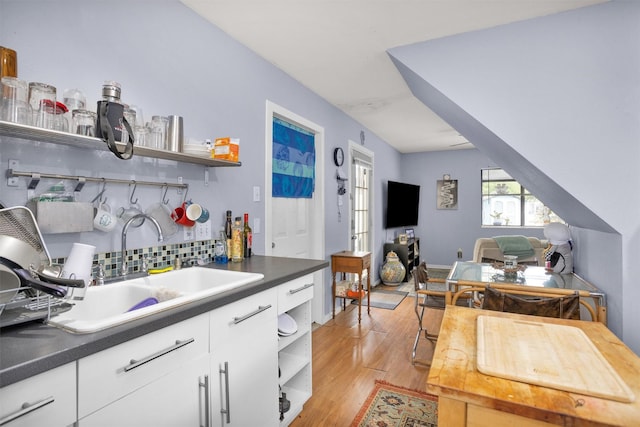 kitchen featuring open shelves, light wood-style floors, dark countertops, backsplash, and a sink