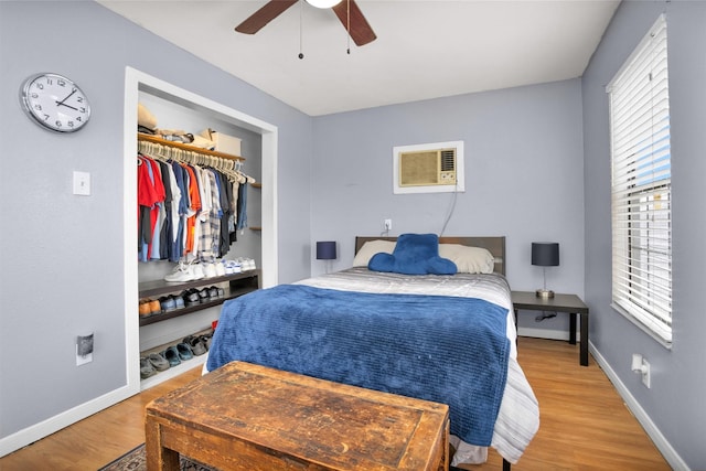 bedroom with wood finished floors, a closet, ceiling fan, a wall mounted AC, and baseboards