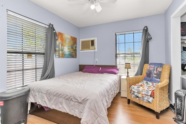 bedroom with ceiling fan, a wall unit AC, and wood finished floors