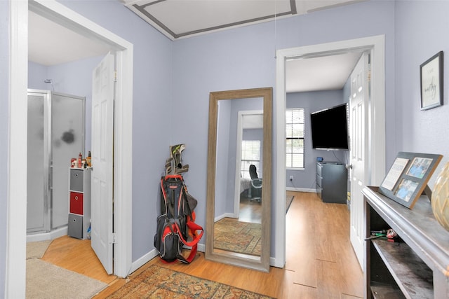 corridor featuring attic access, light wood-style flooring, and baseboards
