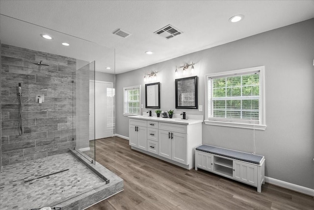 bathroom featuring a tile shower, double vanity, visible vents, recessed lighting, and wood finished floors