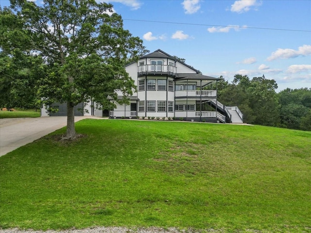 victorian home featuring stairway, a balcony, a front yard, and concrete driveway