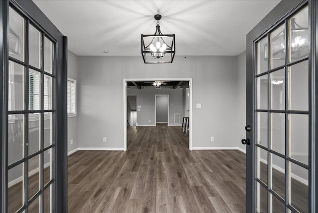 interior space featuring baseboards, wood finished floors, ceiling fan with notable chandelier, and french doors