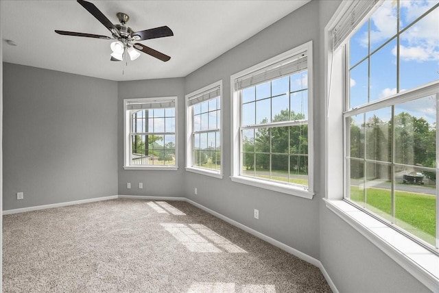 carpeted empty room with a healthy amount of sunlight, a ceiling fan, and baseboards