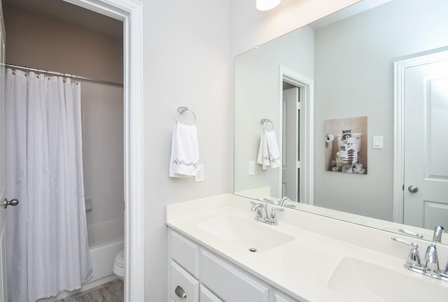 bathroom featuring double vanity, a sink, shower / bath combo with shower curtain, and toilet