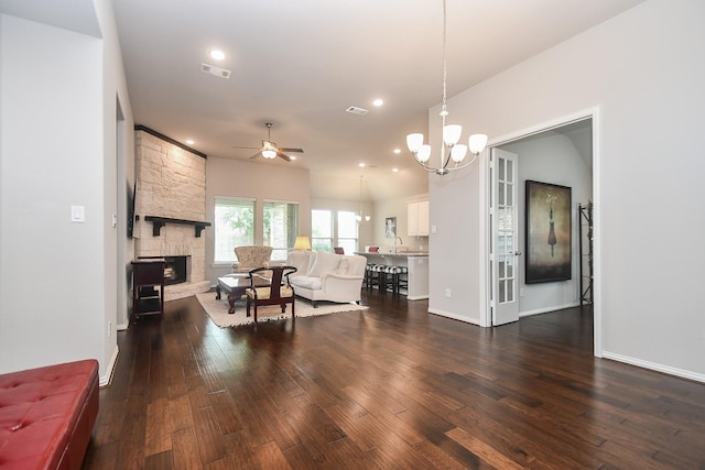 living area with ceiling fan with notable chandelier, dark wood finished floors, a stone fireplace, and visible vents