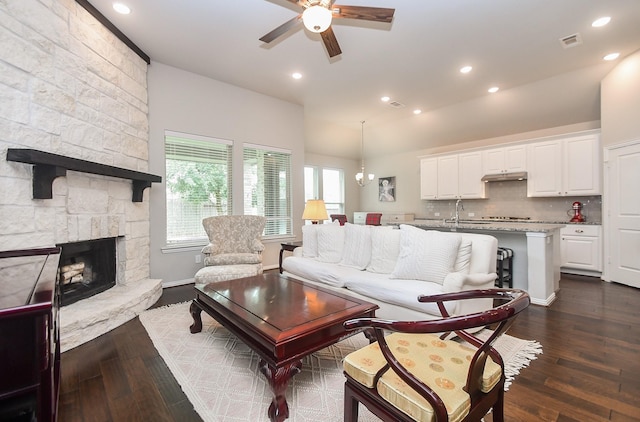 living room with visible vents, ceiling fan, a stone fireplace, and dark wood-type flooring